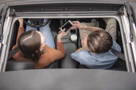 Man and woman in car, female driver hands the male passenger her smartphone