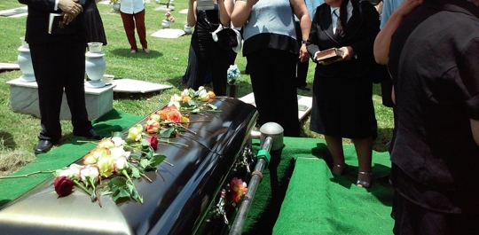 Mourners stand around a closed casket at a funeral