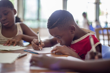 Young boy sits at desk in school surrounded by classmates