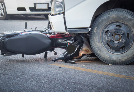 Accident scene involving a motorcycle crashed under the front of a white truck on a city road