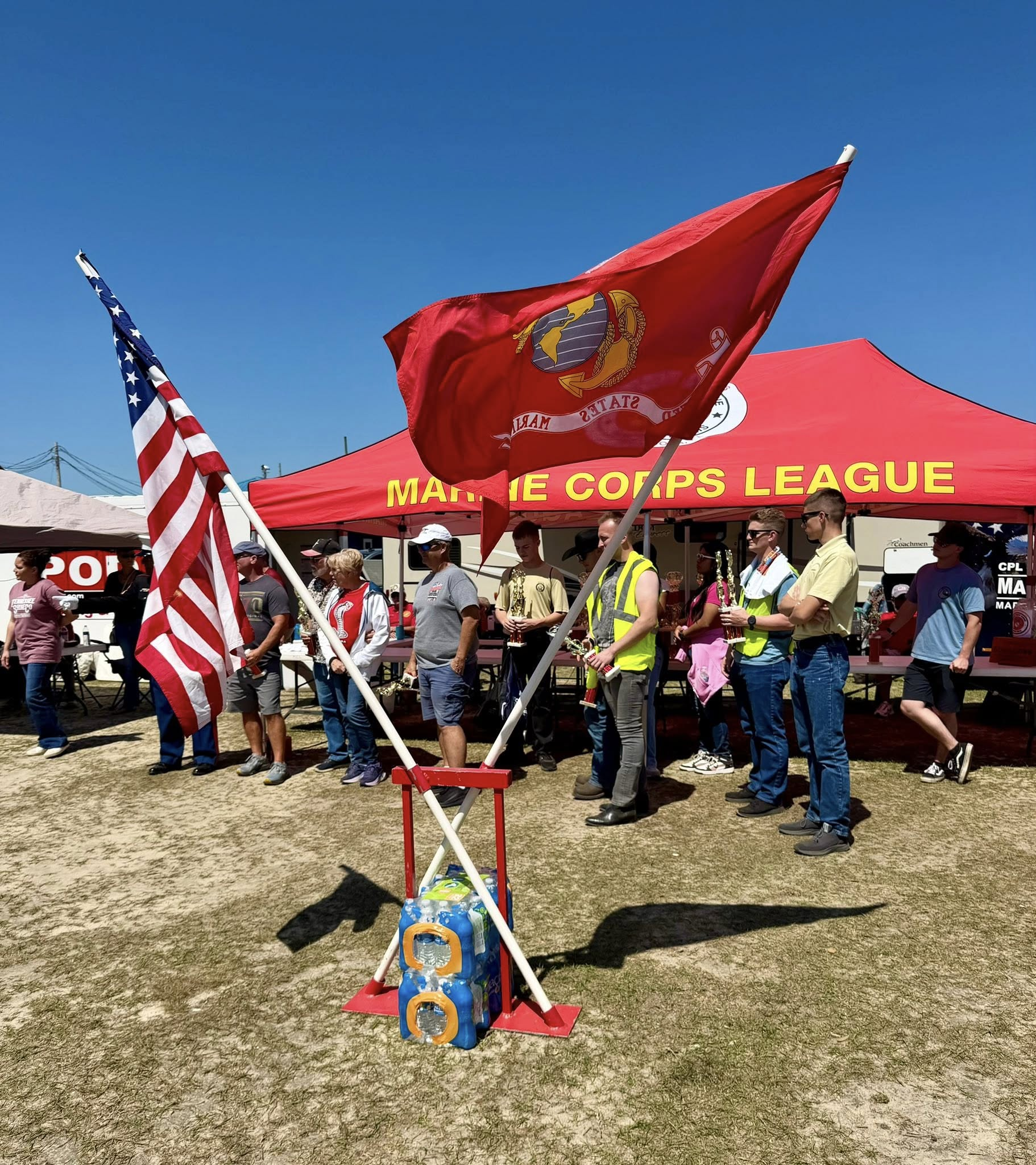 Marine Corps flag and United States flag crossing over with people in the background